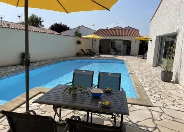 La terrasse avec piscine découverte, un salon de jardin métallique et un parasol sur pied.