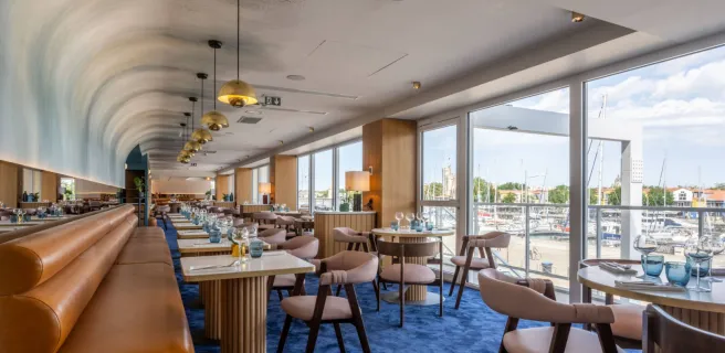 La salle du restaurant, avec ses tables, chaises et banquettes, vue sur les bateaux du bassin.